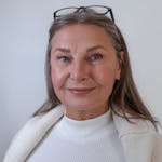 Senior woman with glasses smiling warmly in a cozy white sweater indoors.