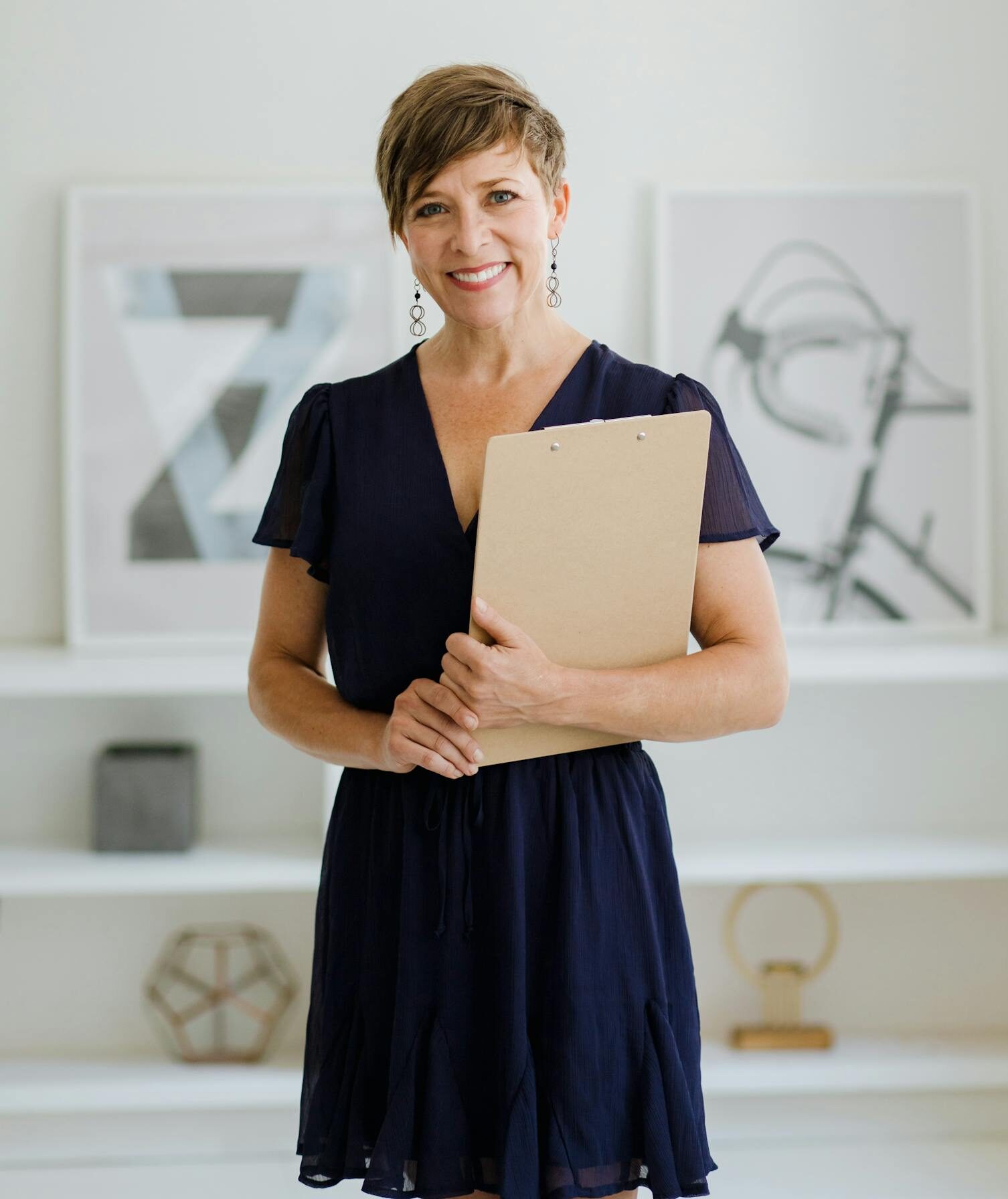 Woman with short hair holding a clipboard in a minimalist indoor setting.